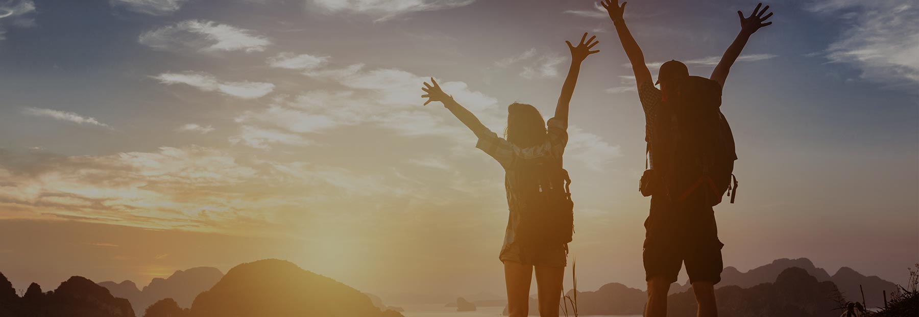 Two hikers raising their arms up in triumph as they look at the sunset