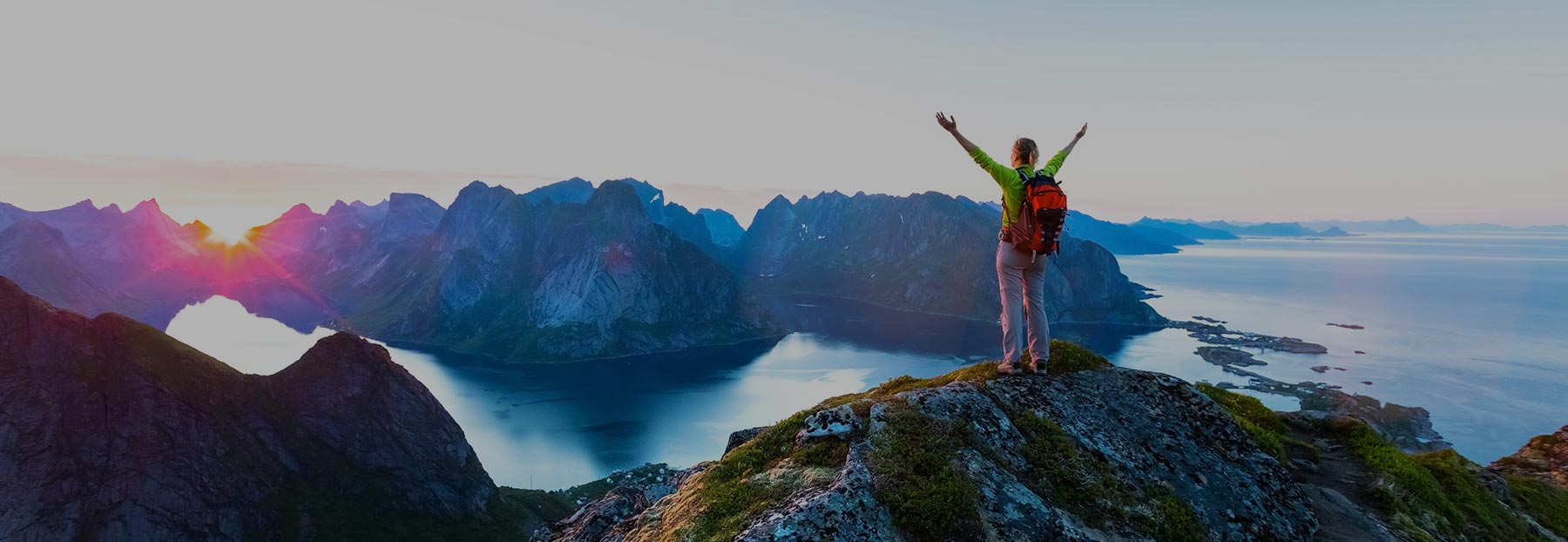 Hiking woman holding her hands up at the peack of a mountain overlooking the ocean