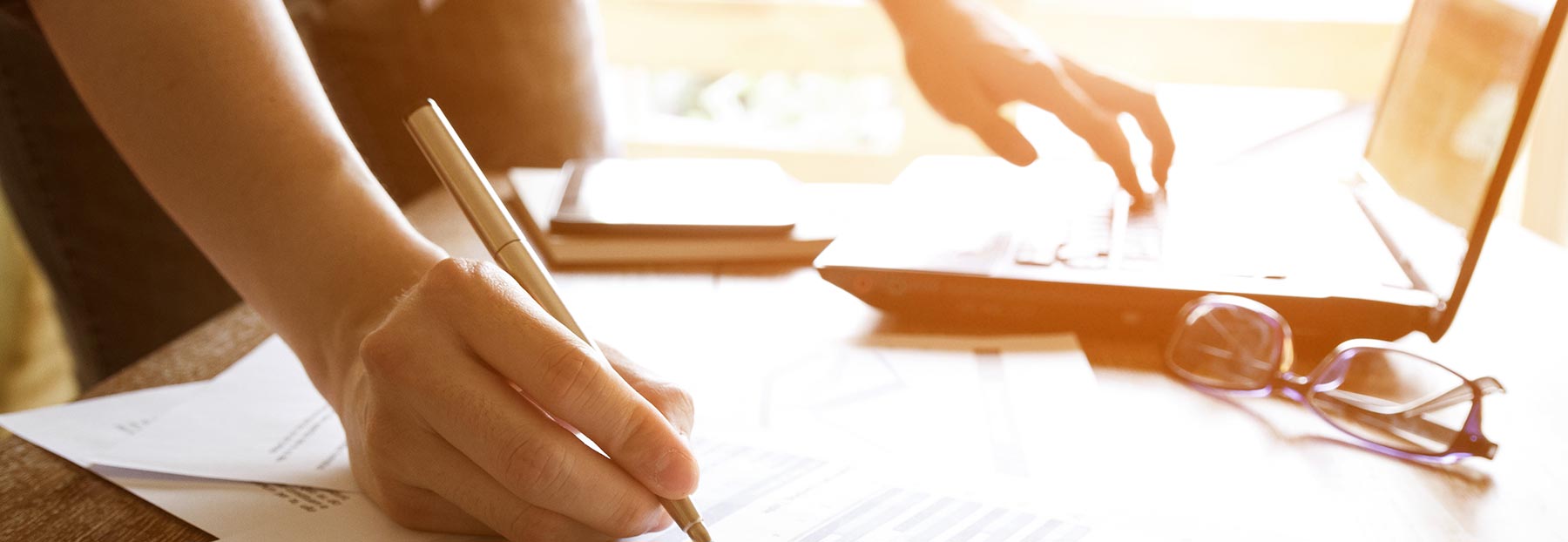 Close up of person writing down information while working on their laptop