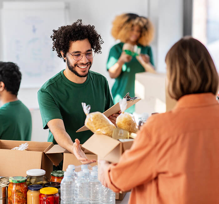 Smiling volunteer handing food package to a person at a community center.