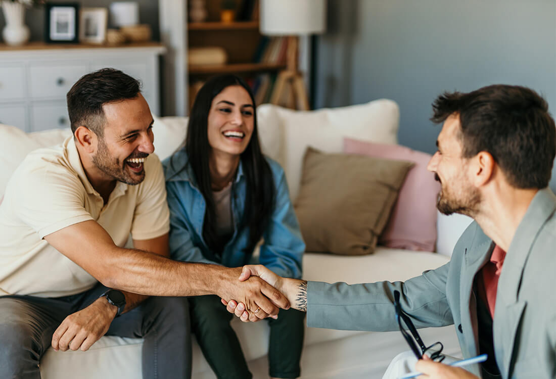 Smiling couple meeting with advisor in a cozy living room setting.
