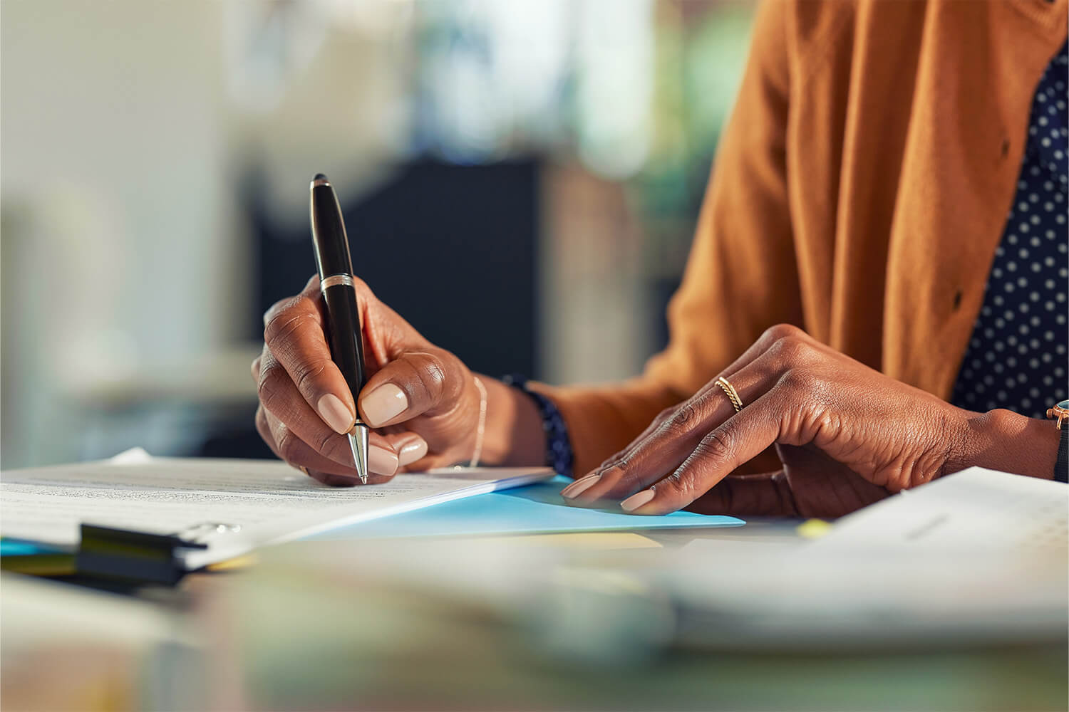 Close-up of hand signing documents on a desk with a pen.