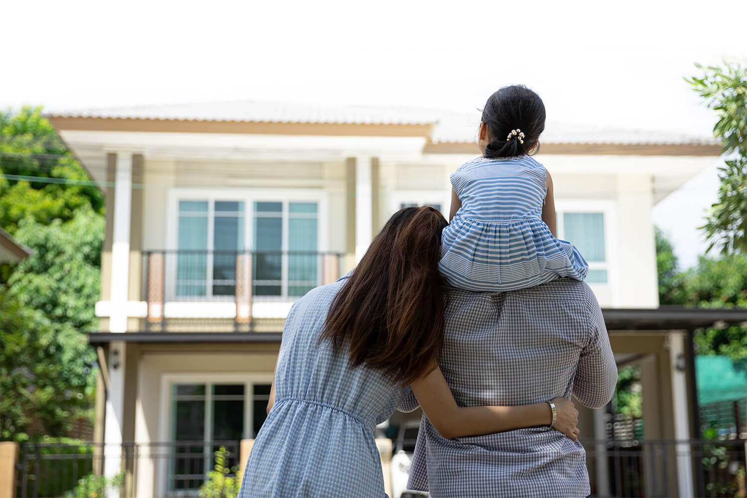 Family embracing in front of a two-story building with large windows.