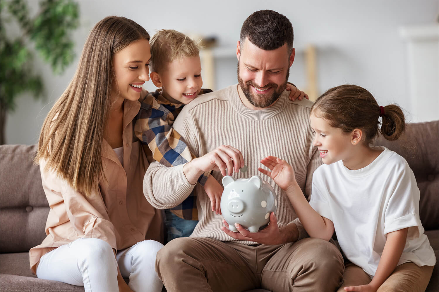 Family sitting on a couch, adding coins to a piggy bank.