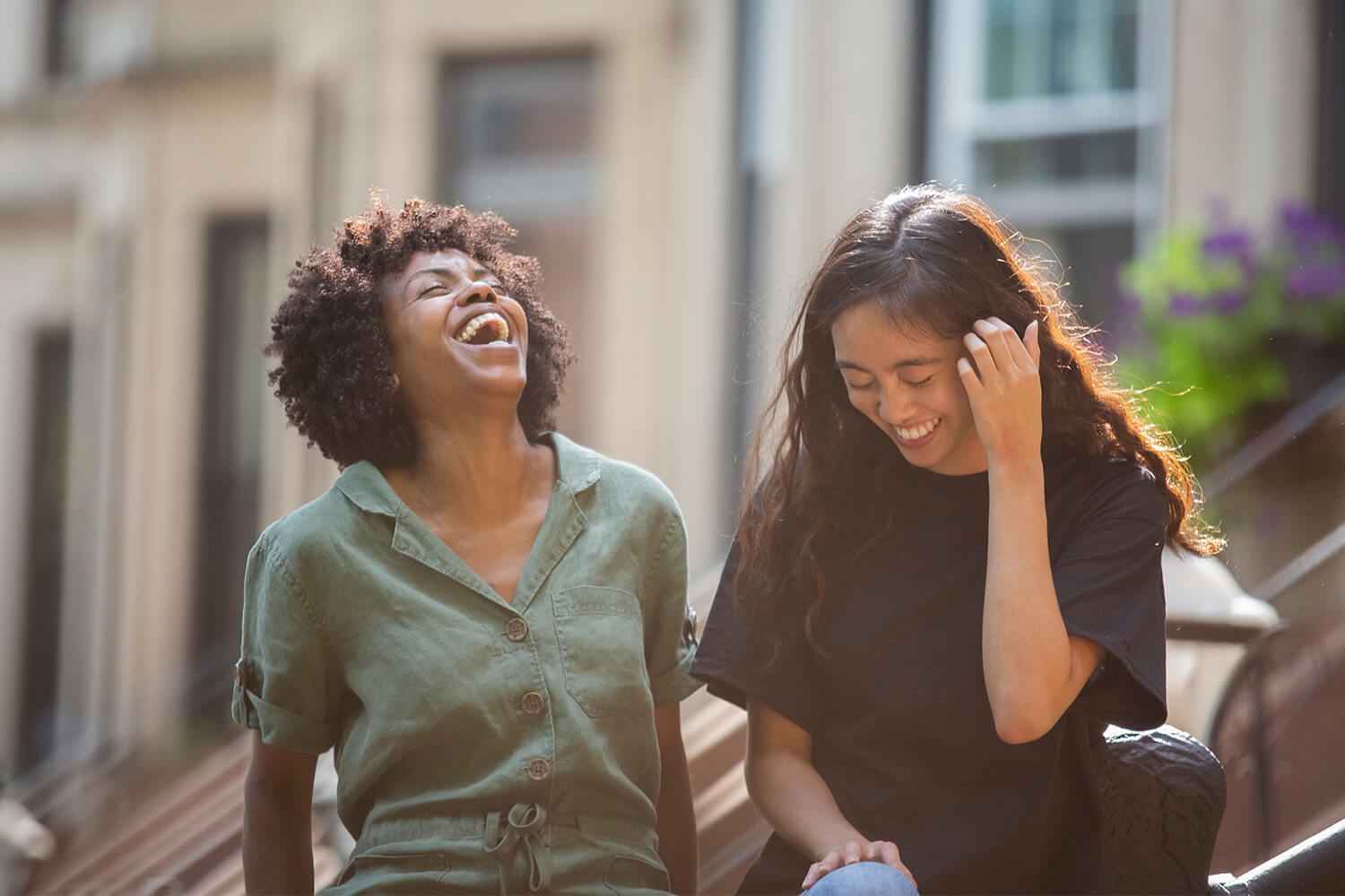 Two friends laughing and sitting on steps outside a building.
