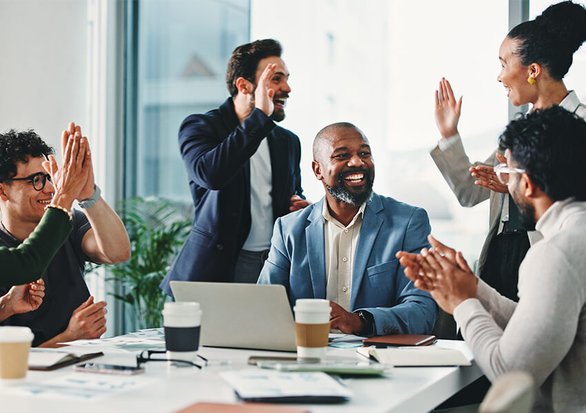 Diverse group of professionals celebrating success with high fives in modern office space.