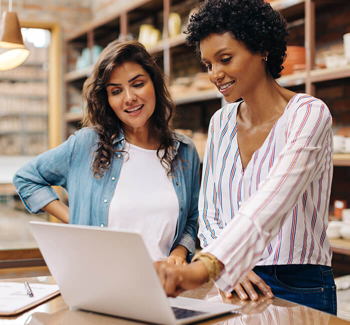 Two women smiling and looking at a laptop in a modern living space.
